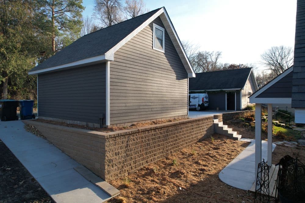 Side view of a gray house with a landscaped yard and retaining wall, highlighting exterior details.