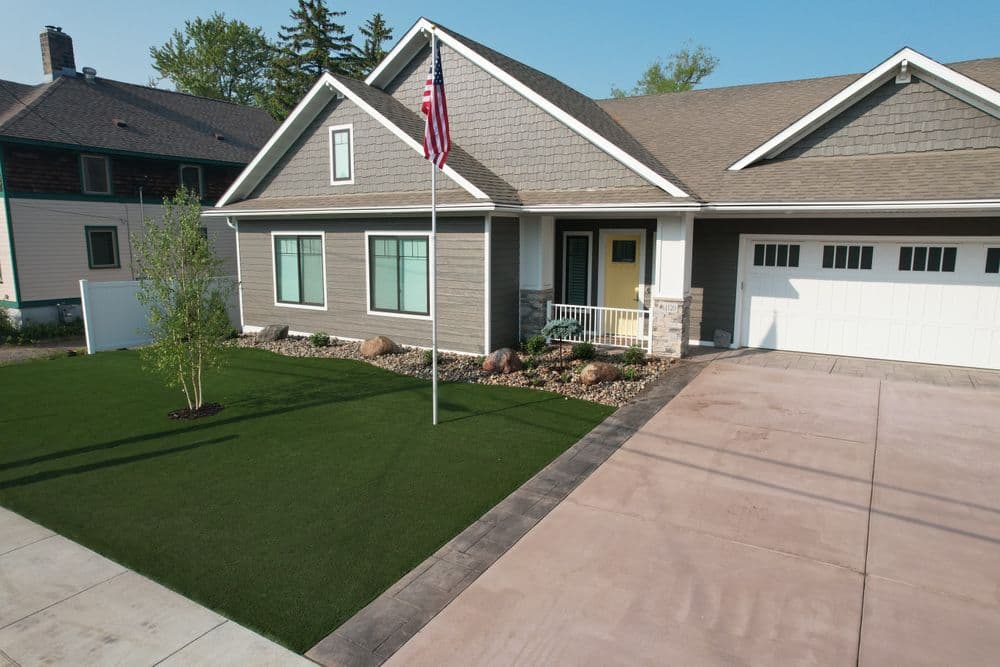 Newly built modern house with American flag, landscaped yard, and concrete driveway.